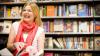 Woman smiling off camera, while opening a book in front of a book shelves.