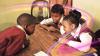 A group of three children from South Africa sitting inside a classroom at their study desk and chatting